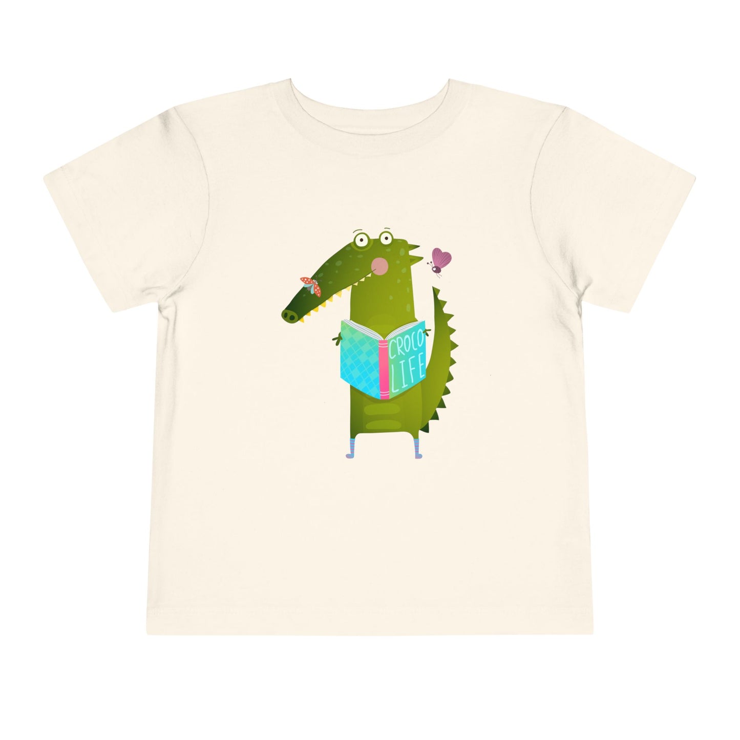 Beige t-shirt with a cartoon crocodile reading a Croc Life book amongst sweet insects 