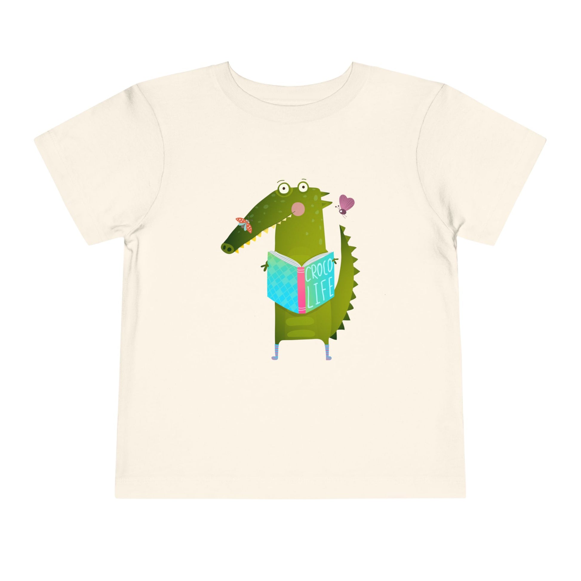 Beige t-shirt with a cartoon crocodile reading a Croc Life book amongst sweet insects 