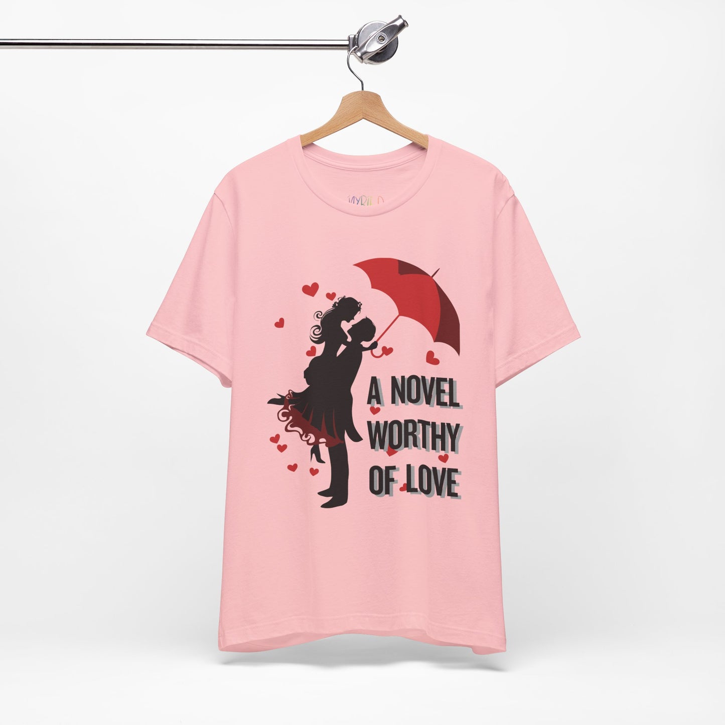 Pink t-shirt with a black graphic design of a man holding a woman under a red umbrella, sprinkled with hearts and text 'A Novel Worthy of Love' 
