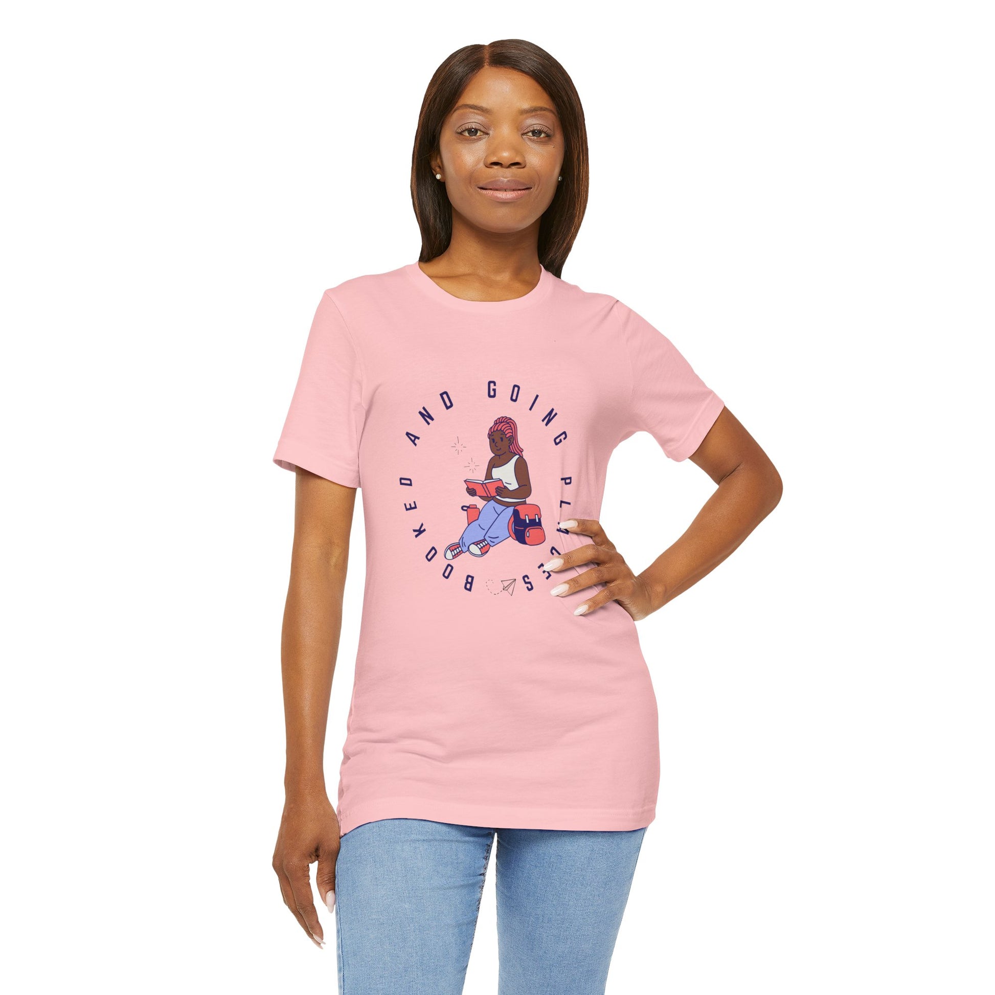 Woman wearing a pink t-shirt with graphic design of a school girl sitting with a book and text 'Booked And Going Places'
