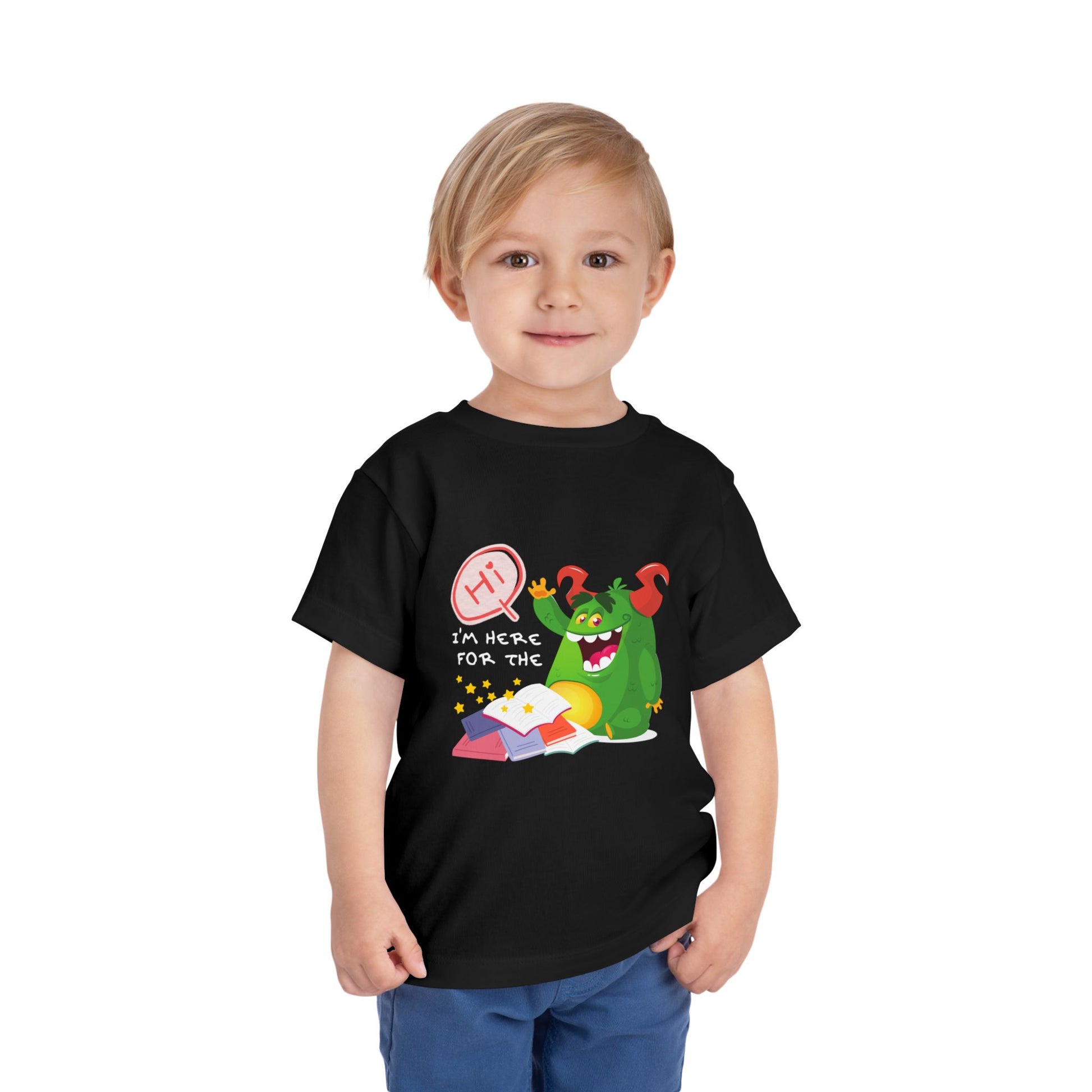 Child wearing a black toddler t-shirt with a waiving green monster and text 'Hi, I'm here for the' and then a pile of books