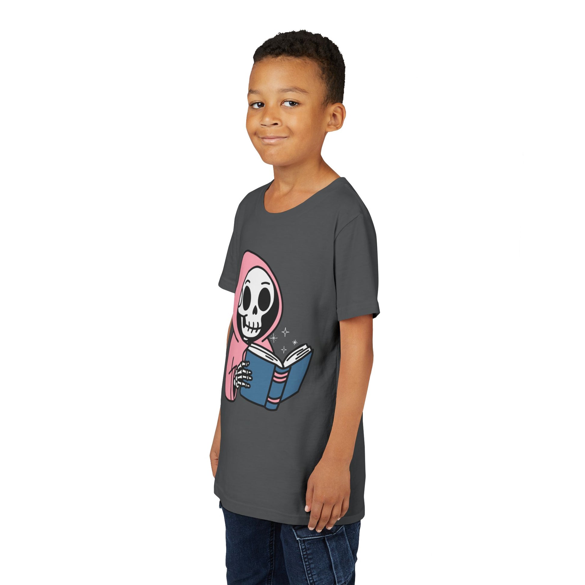 Boy wearing a gray t-shirt with a cartoon skeleton wearing a pink hoodie and reading a book