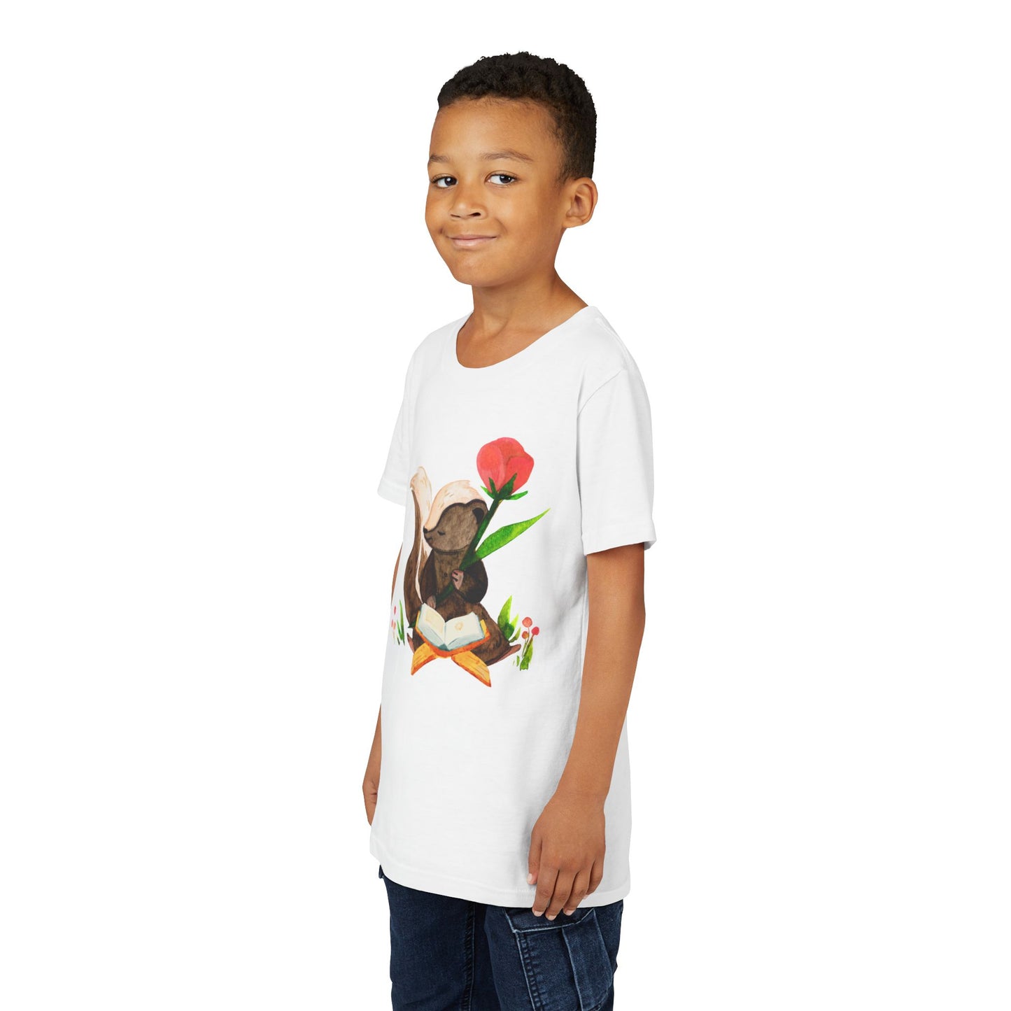 Boy wearing a white t-shirt with a graphic of a skunk reading a book in a patch of flowers