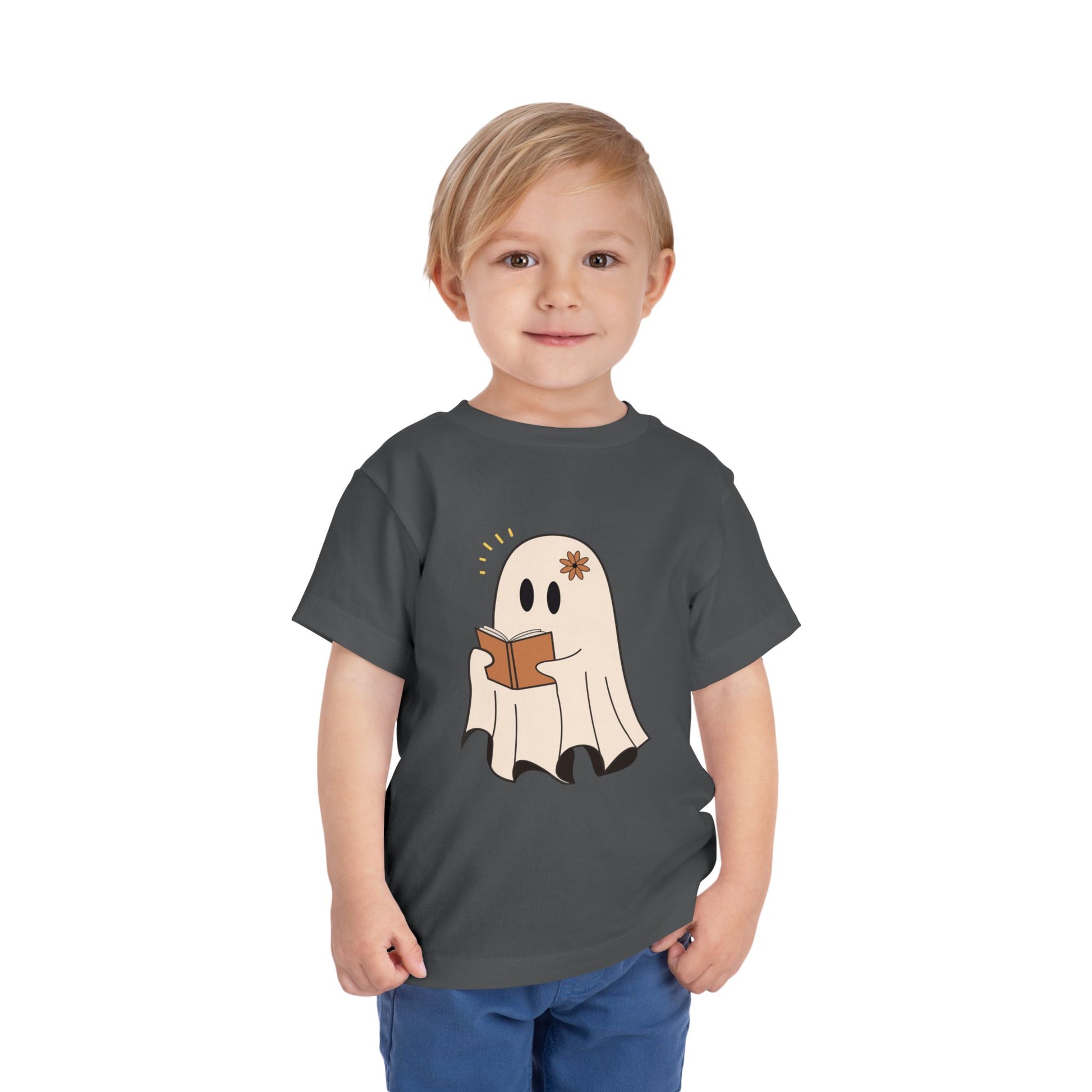 Child wearing a gray toddler t-shirt with a cartoon ghost reading a book 