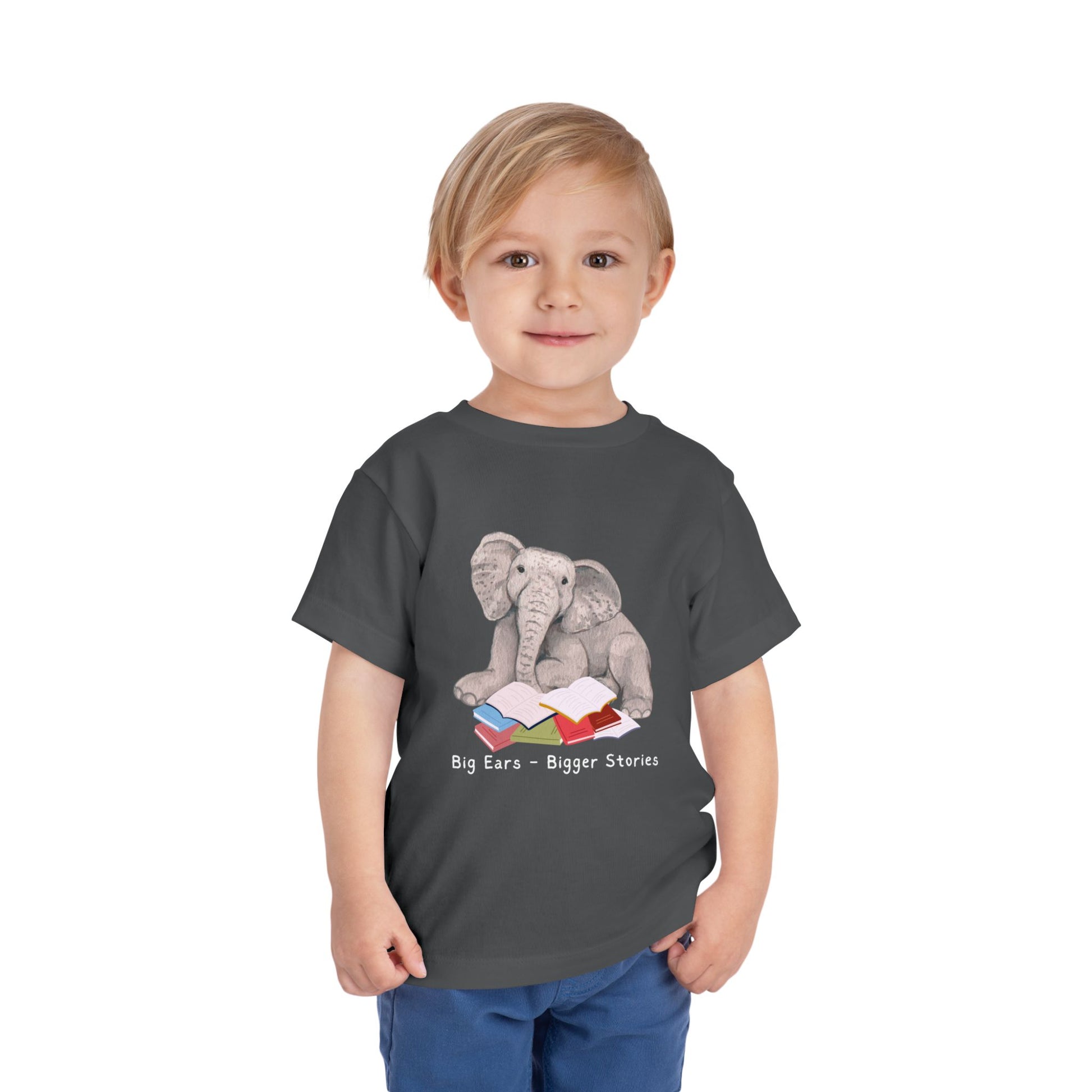Toddler wearing a gray t-shirt with an elephant reading a stack of books and text 'Big Ears - Bigger Stories' 