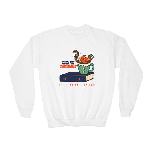 White sweatshirt with an elf splashing upside down in a mug of hot chocolate on a book, text 'Cozy Up Buttercup, It's Book Season'