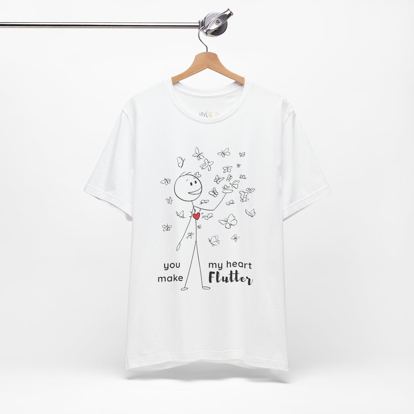 White t-shirt with a stick figure surrounded by butterflies and a red heart beating on his chest, text 'You Make My Heart Flutter'