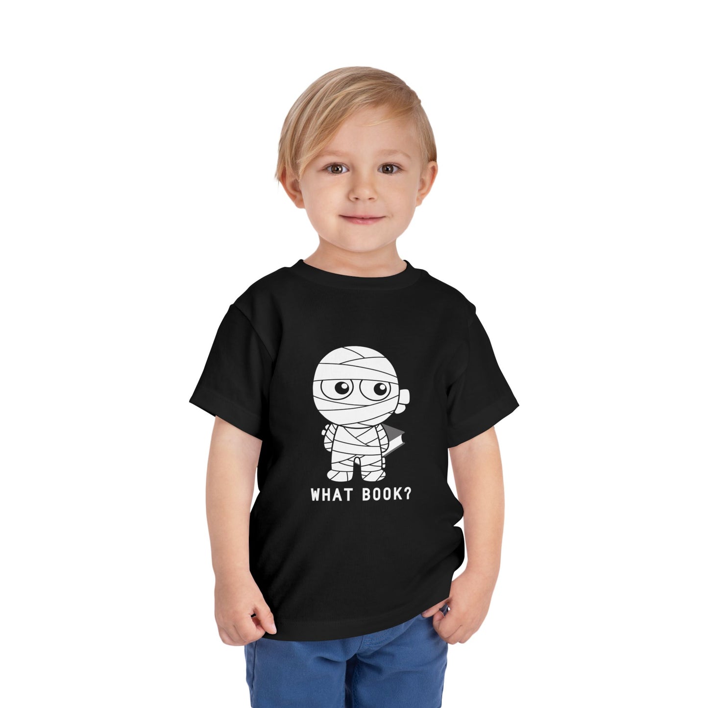 Toddler wearing a toddler t-shirt with a sheepish mummy holding a book behind it's back and text 'WHAT BOOK?' 
