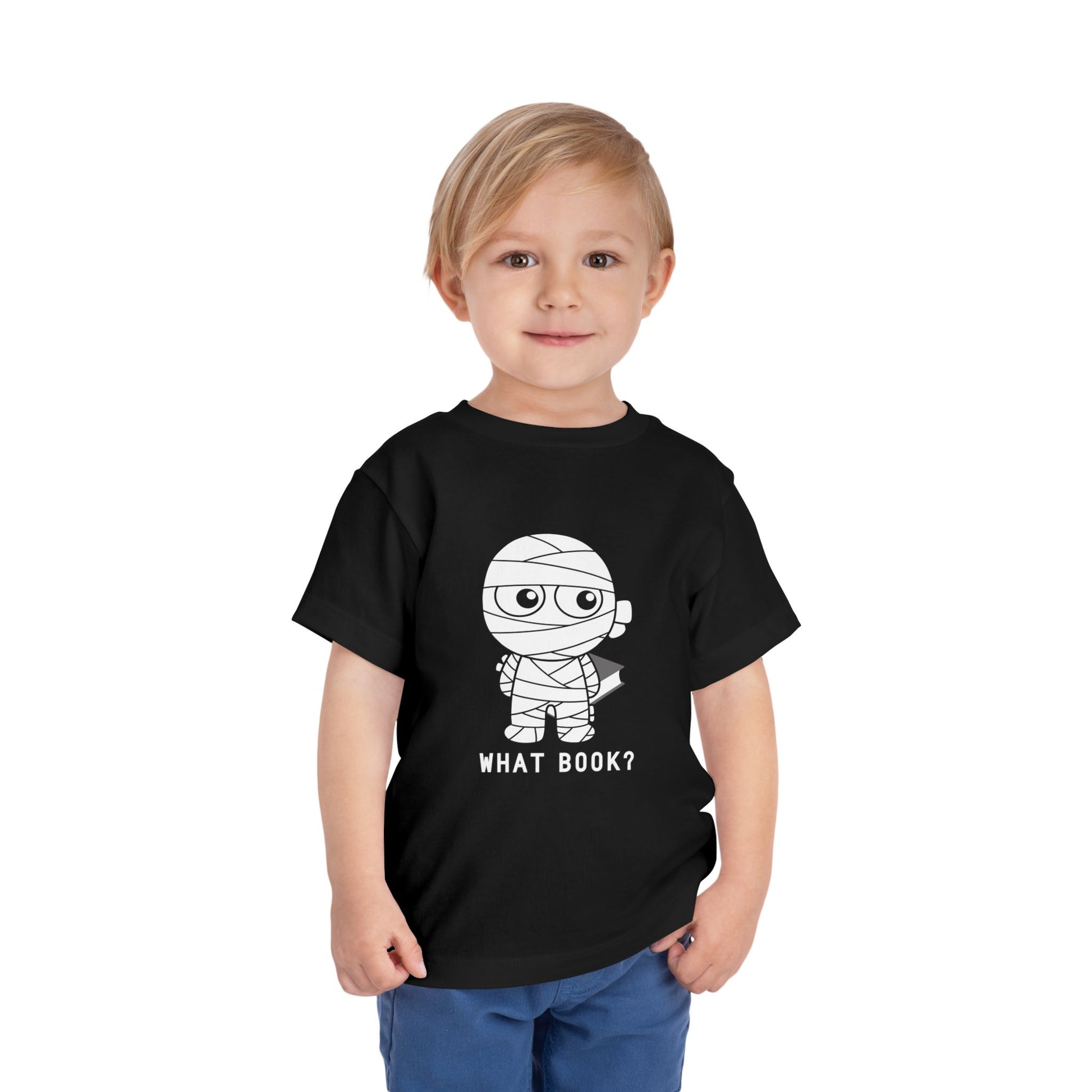Toddler wearing a toddler t-shirt with a sheepish mummy holding a book behind it's back and text 'WHAT BOOK?' 