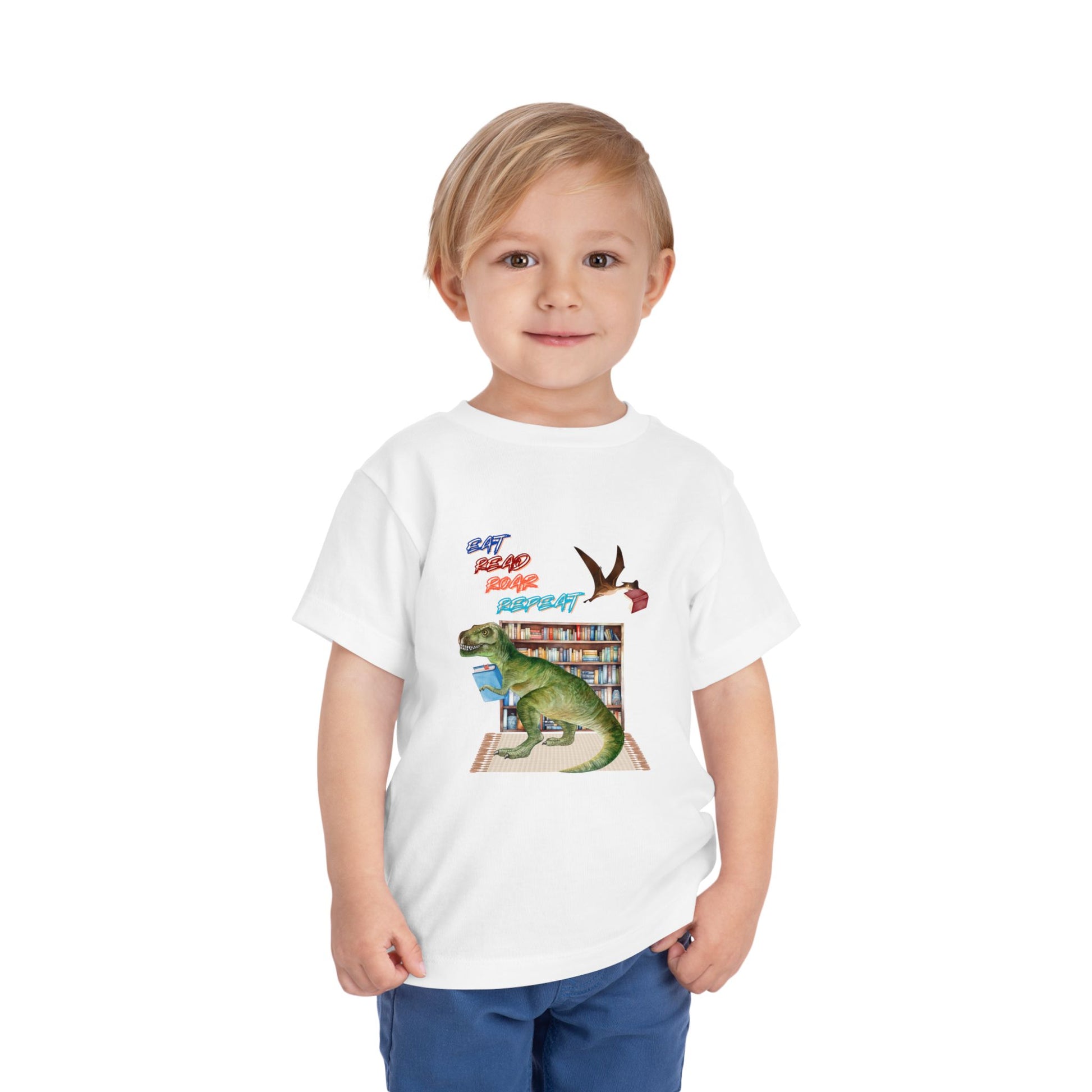 Child wearing a white toddler t-shirt with a t-rex dinosaur checking out a book at the library, a tera dactyl flying overhead with a book and text 'Eat, Read, Roar, Repeat' 