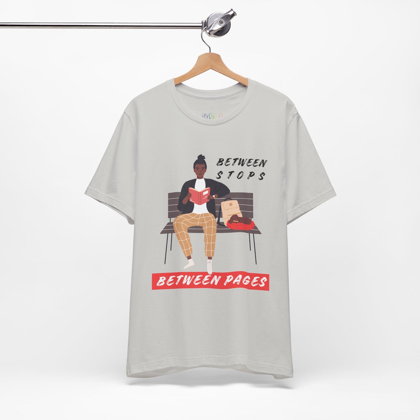 Gray t-shirt with a graphic of a person sitting on a bench reading a book, with text 'Between Stops Between Pages' 