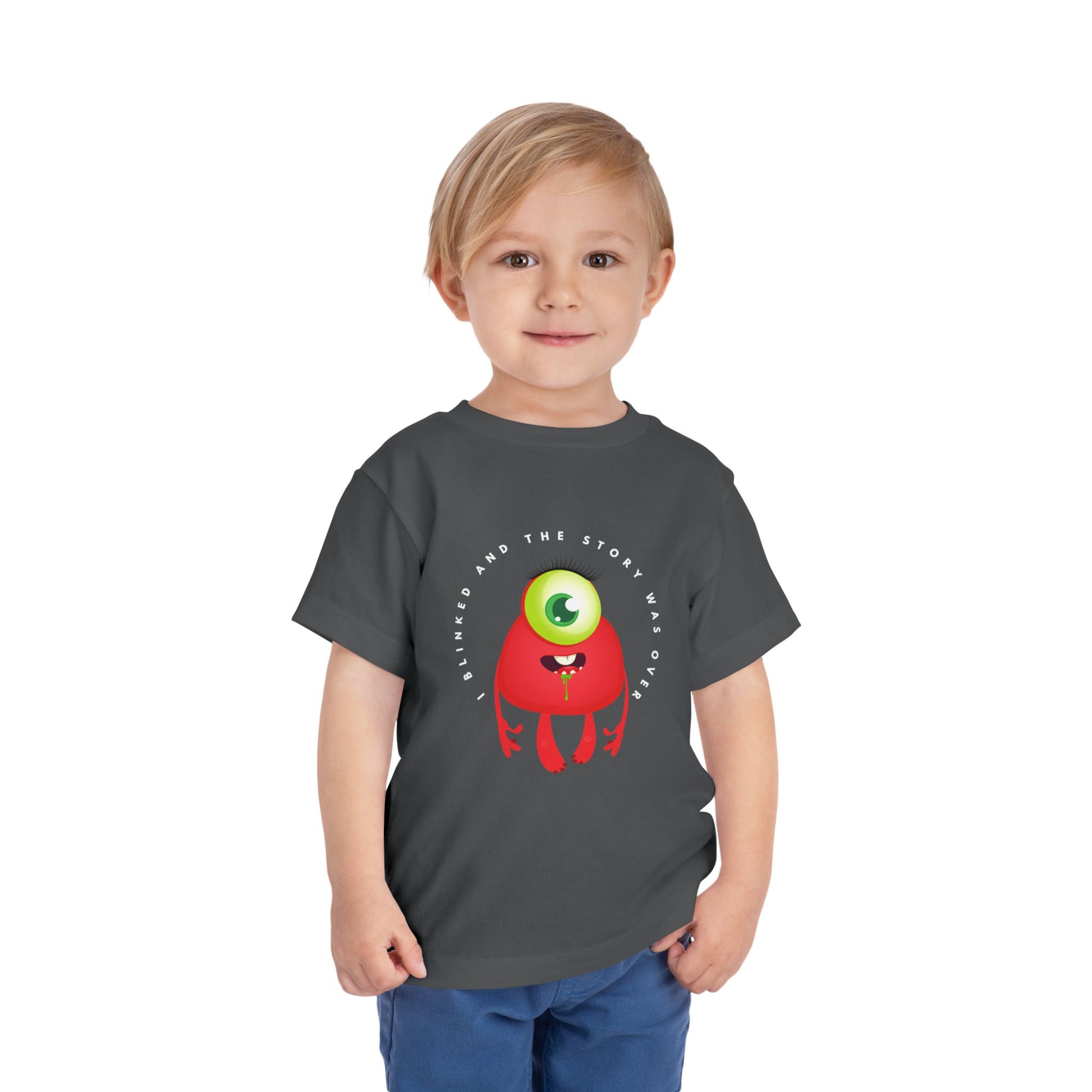Child wearing a gray toddler t-shirt with a drooling, one eyed, red monster graphic and text 'I blinked and the story was over'