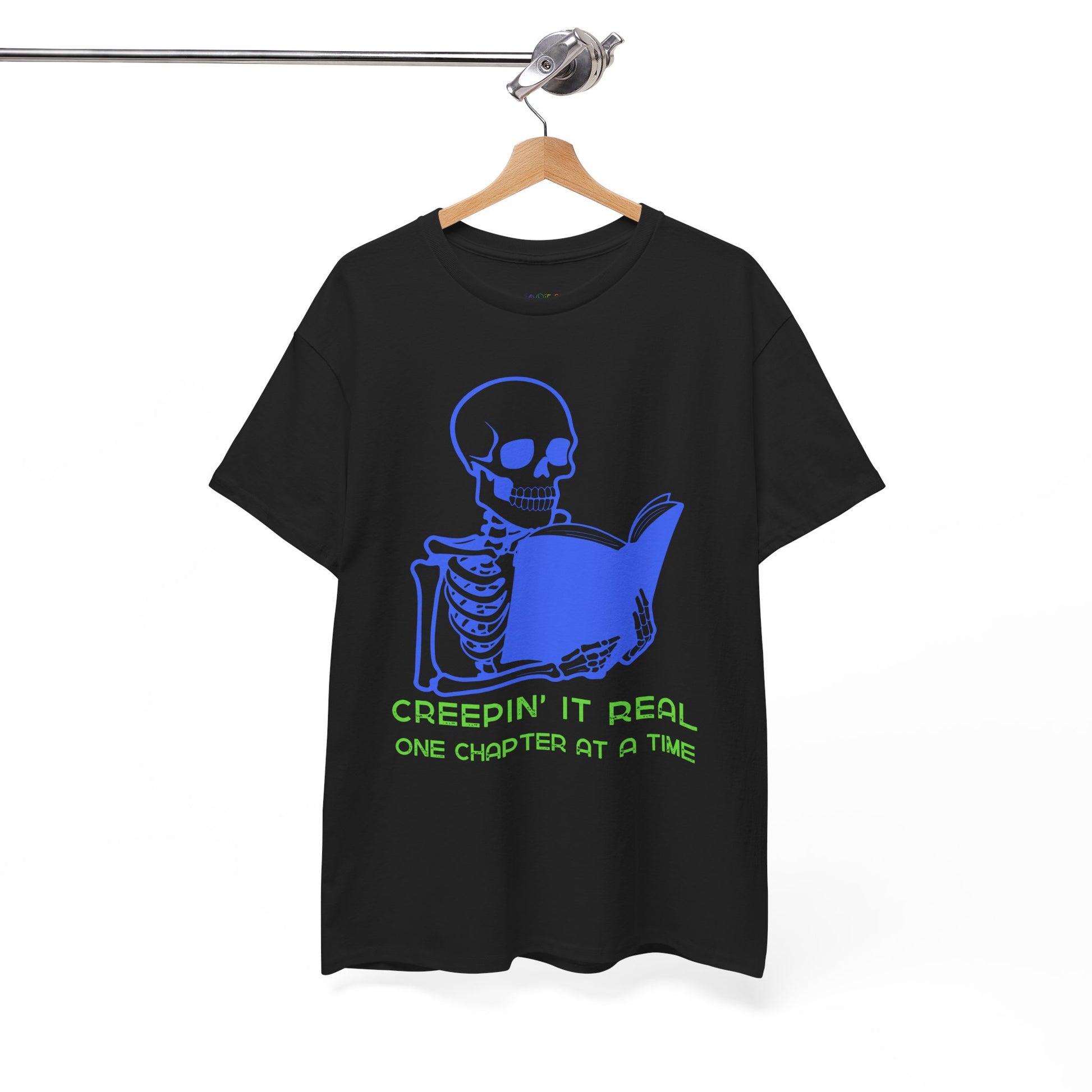 Black t-shirt with blue skeleton graphic reading a book and green text 'Creepin' It Real One Chapter At A Time' on a hanger against a white background