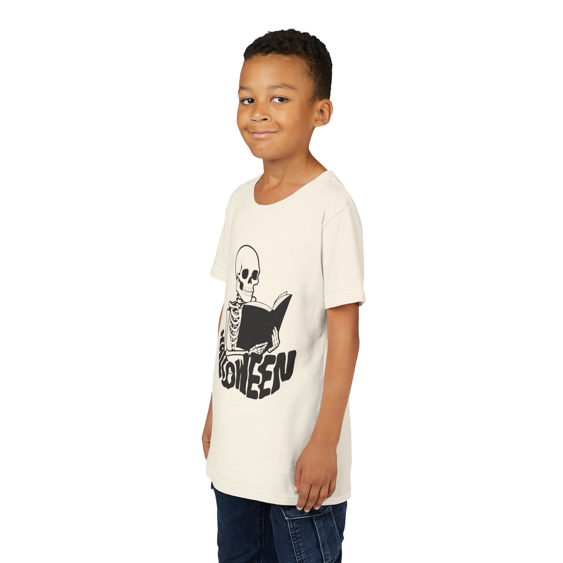 Boy wearing a beige t-shirt with a black skeleton reading a book and 'Halloween' text spelled out in a spooky font