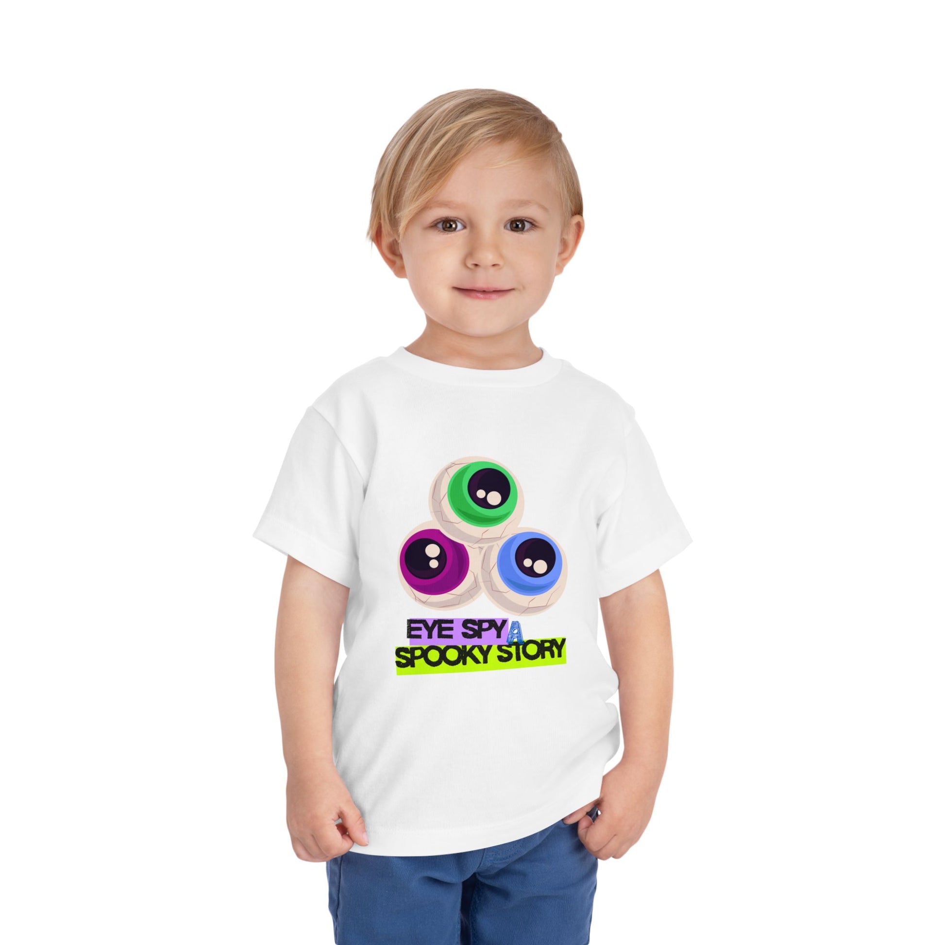 Child wearing a white toddler t-shirt with colorful eyeballs and text "Eye Spy A Spooky Story' on a white background