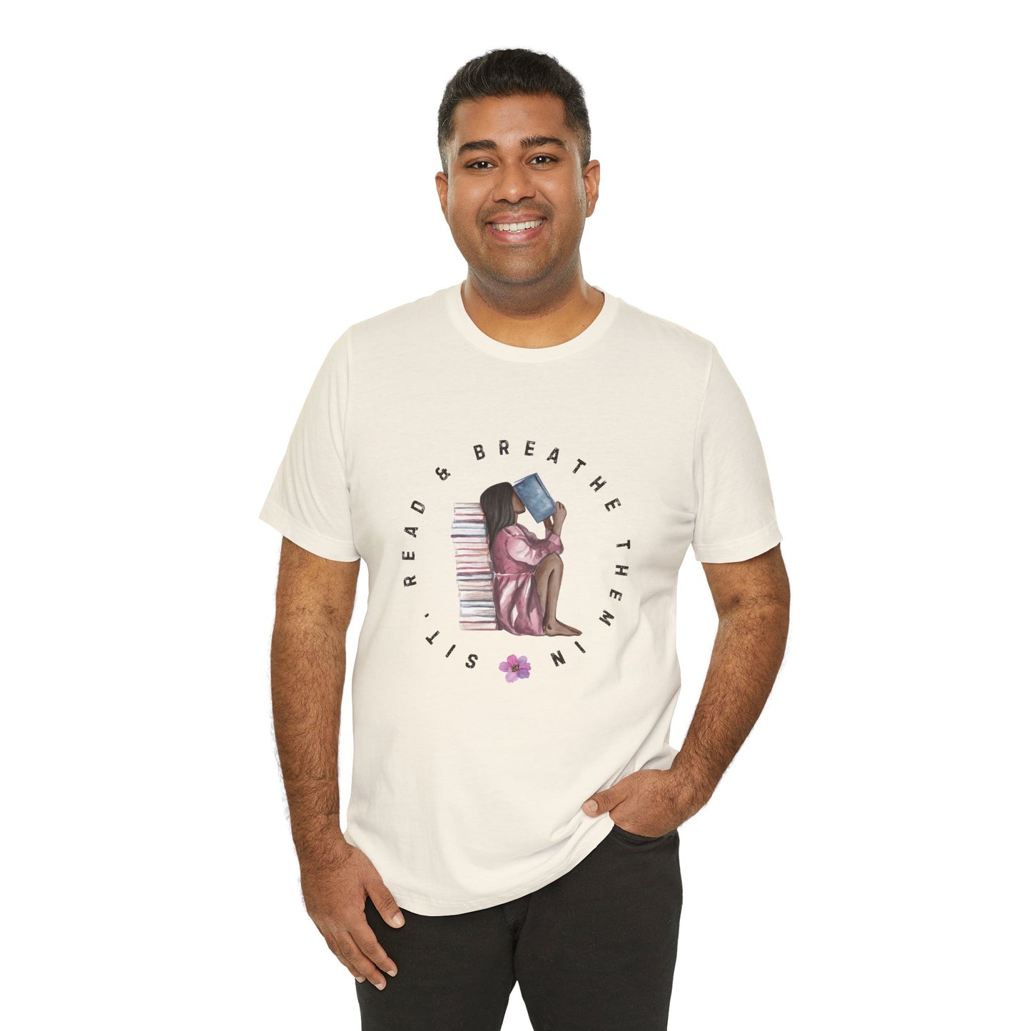 Man wearing a beige t-shirt with graphic design of a girl sitting on the ground against a stack of books, inhaling the book she's reading and text 'Sit, Read & Breathe Them In'