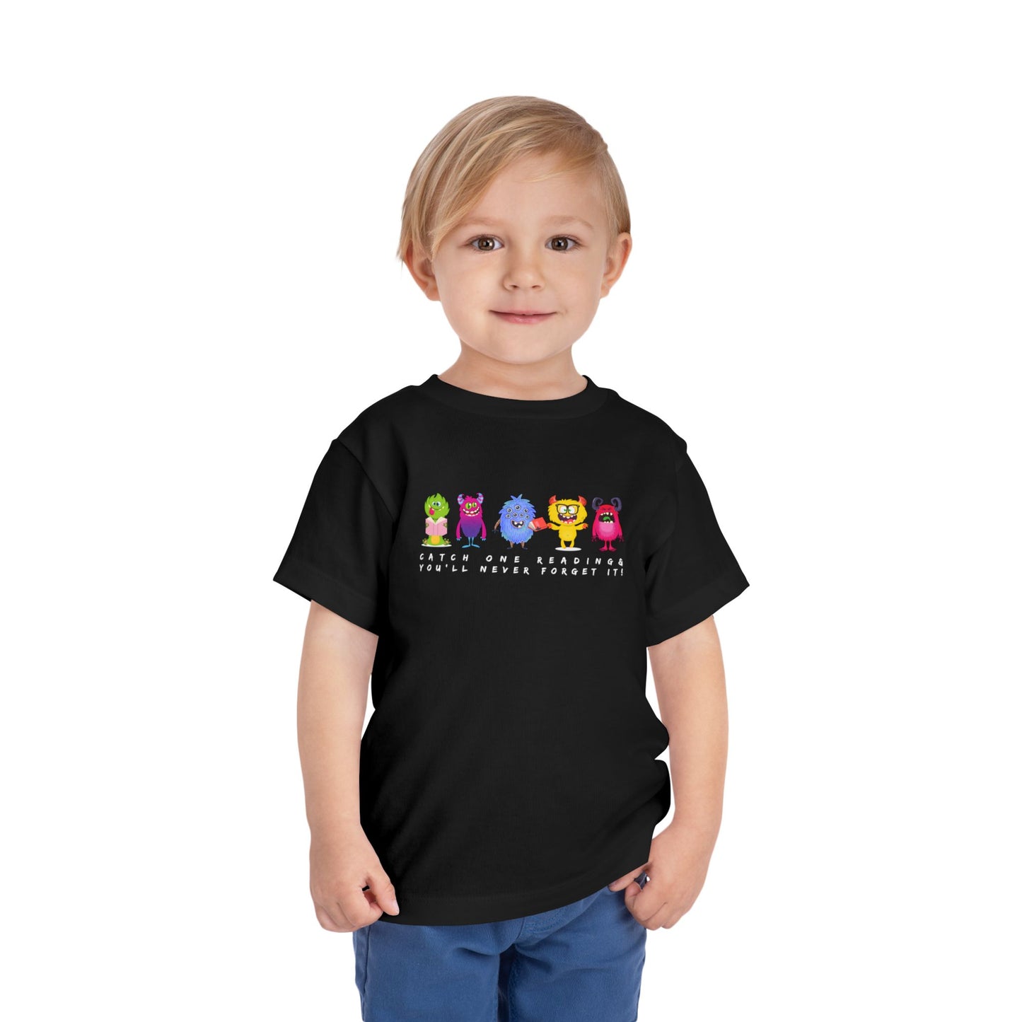 Child wearing a black toddler t-shirt with colorful monsters all lined up in a row and text 'Catch One Reading & You'll Never Forget It!' 