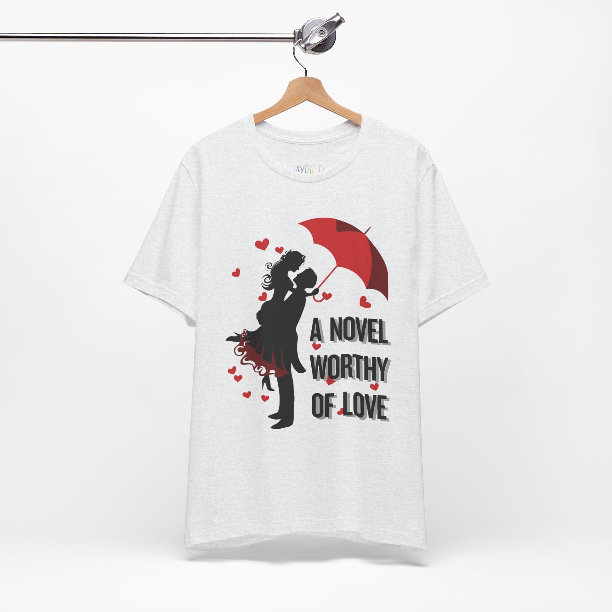 Ash t-shirt with a black graphic design of a man holding a woman under a red umbrella, sprinkled with hearts and text 'A Novel Worthy of Love' 