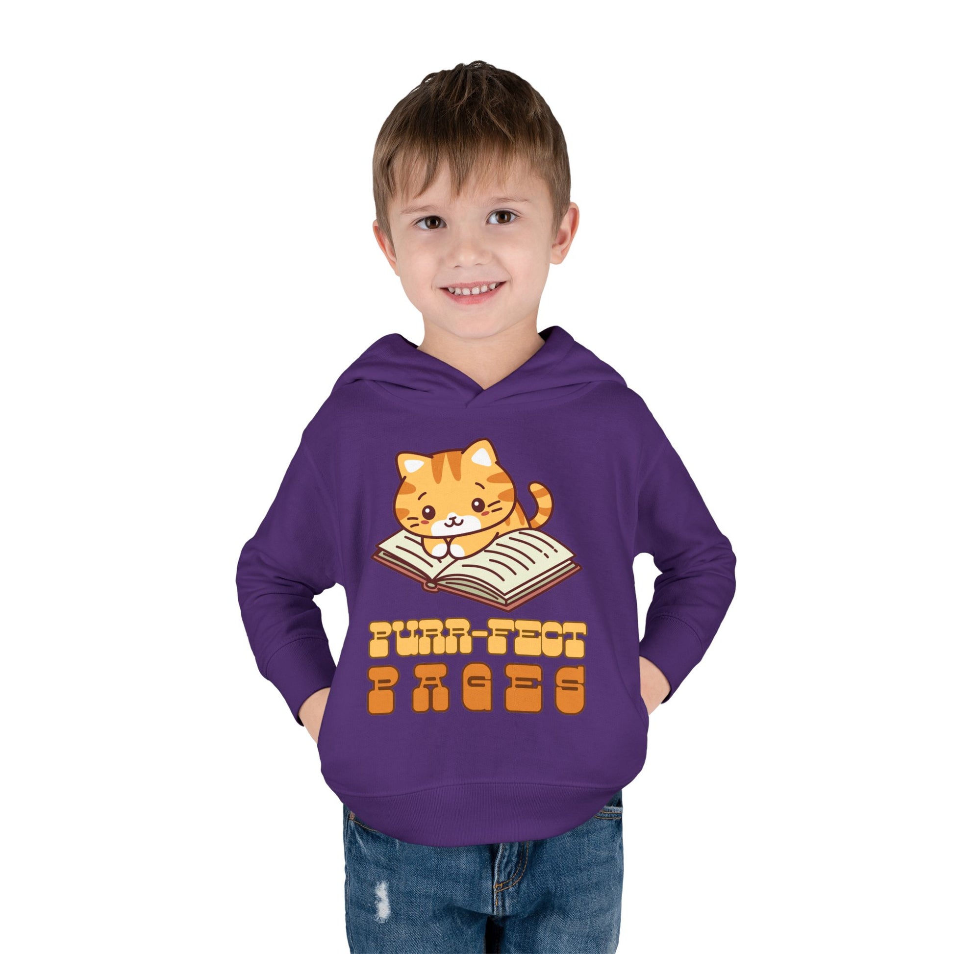 boy wearing a purple toddler hoodie with a cat graphic laying on a book and retro text 'Purr-fect Pages' 