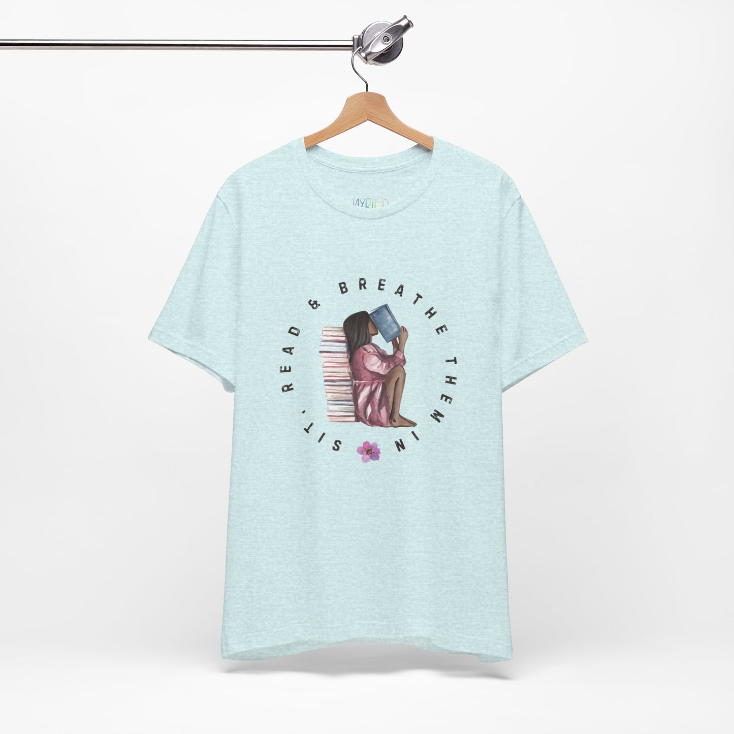 Light blue t-shirt with graphic design of a girl sitting on the ground against a stack of books, inhaling the book she's reading and text 'Sit, Read & Breathe Them In'