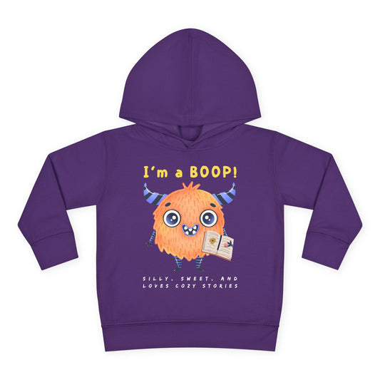 Yellow cartoon monster with big eyes and a sweet smile, holding a book with the words “I’m a Boop” above — printed on a cozy toddler hoodie.