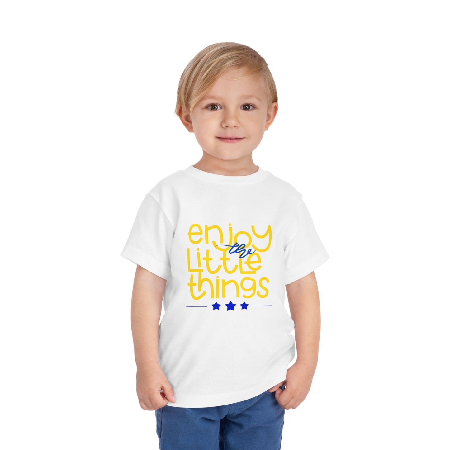 Child wearing a white toddler t-shirt with 'enjoy the little things' text in yellow and blue 