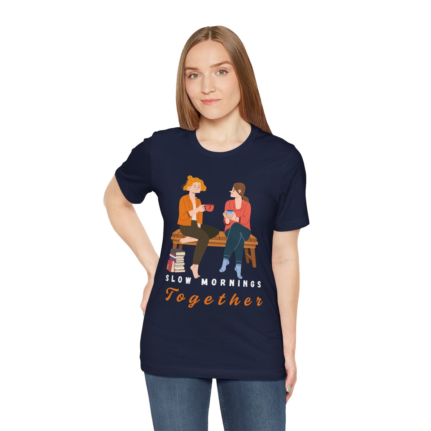 Woman wearing a navy blue t-shirt with graphic of two people sitting on a bench together, hot beverages in their hands, book at their feet and 'Slow Mornings Together' text below the image