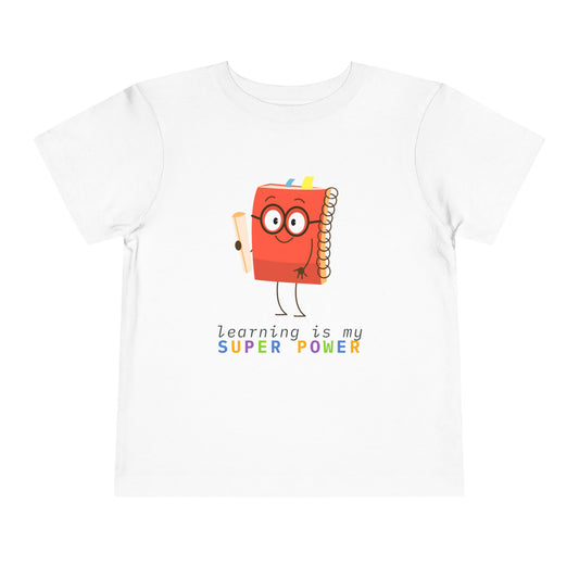 White toddler t-shirt with a cartoon book character and colorful 'learning is my super power' text 