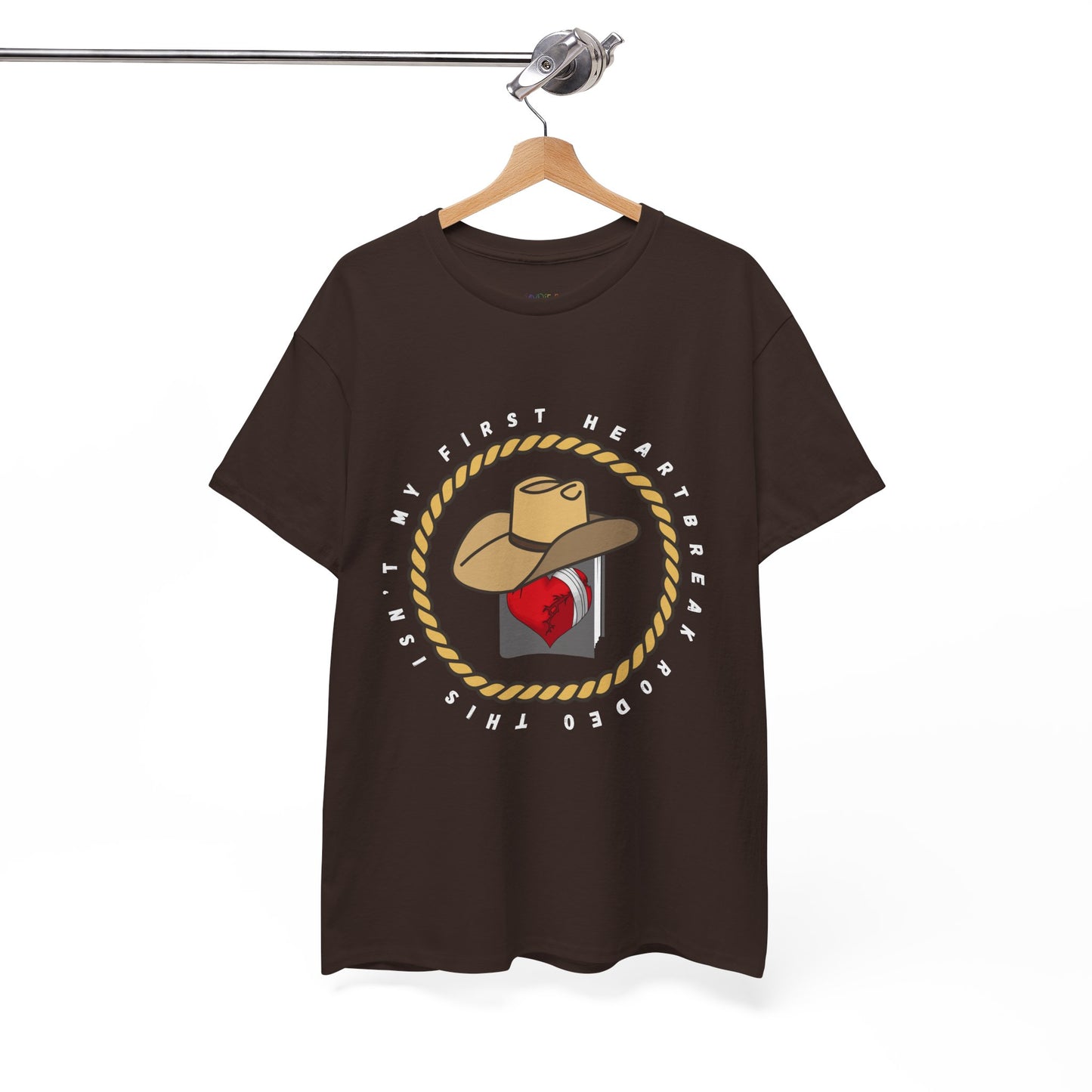 Brown t-shirt with a cowboy hat atop a book with a broken heart, circled by a rope and text 'This Isn't My First Heartbreak Rodeo'