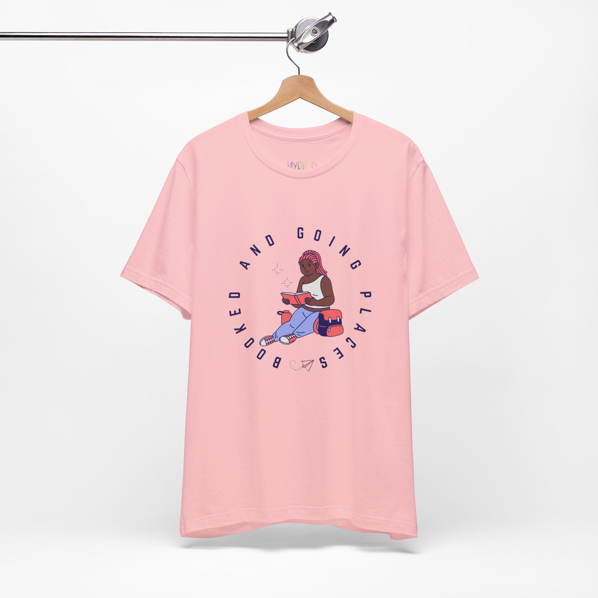 Pink t-shirt with graphic design of a school girl sitting with a book and text 'Booked And Going Places'