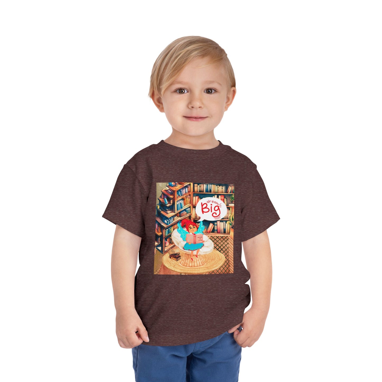 Toddler wearing a maroon t-shirt with a colorful library graphic of a fairy reading a book and thought bubble text 'Dream Big'