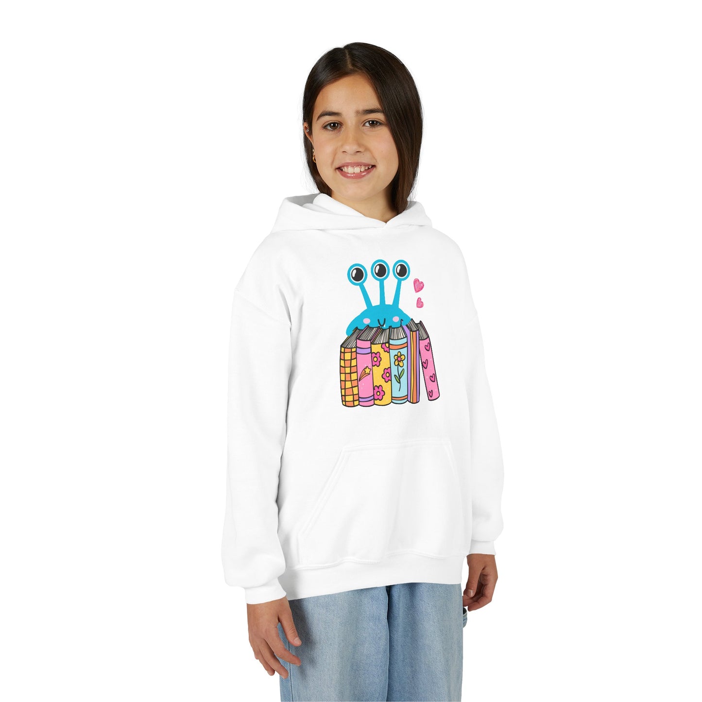 Girl wearing a white hoodie with a three eyed alien standing behind a row of books