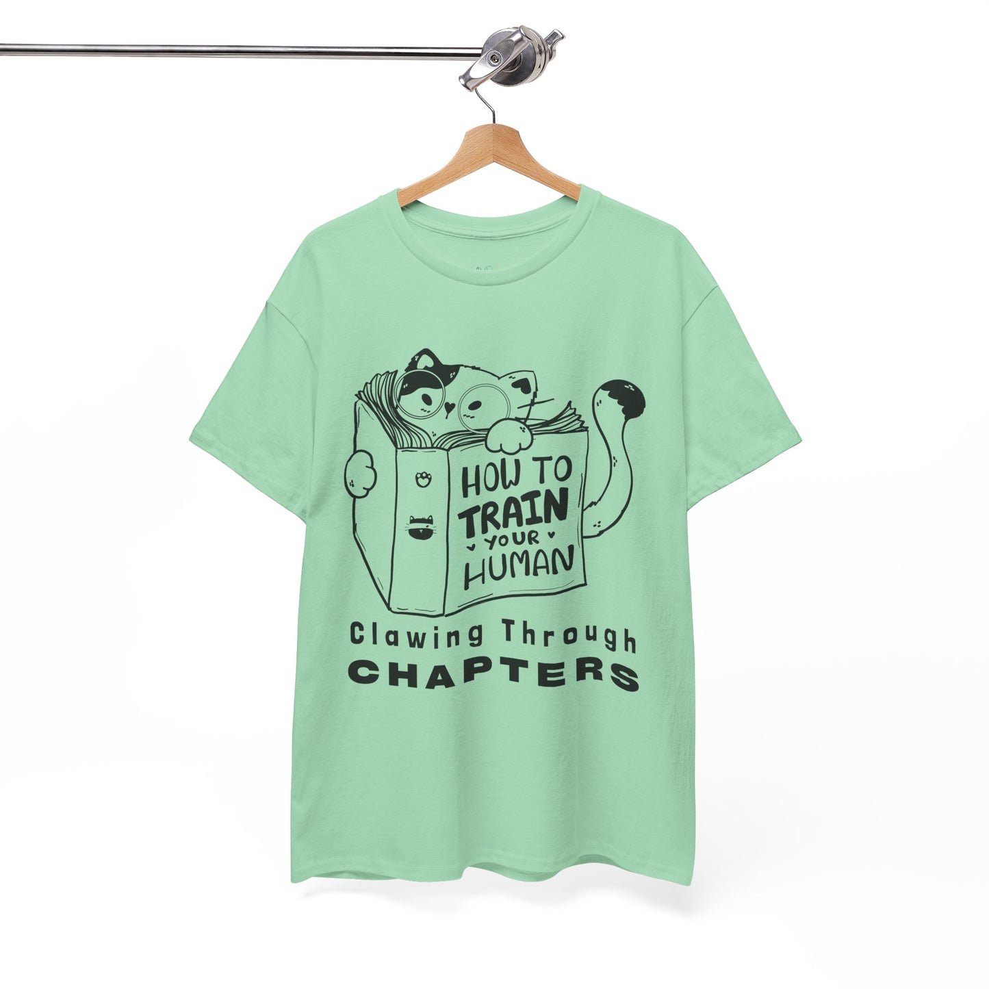 Light green t-shirt with black graphic design of a cat reading a 'How To Train Your Human' book and text 'Clawing Through Chapters'