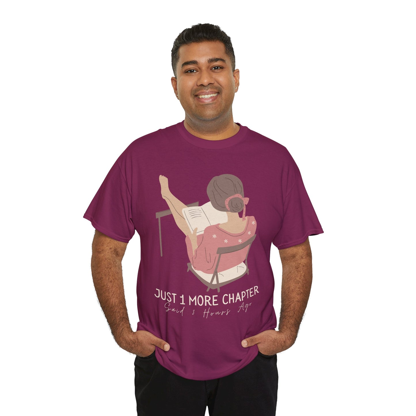 Man wearing a berry t-shirt with a graphic of a person reading a book with her feet propped up and text 'Just 1 More Chapter, Read's Hours Ago' 