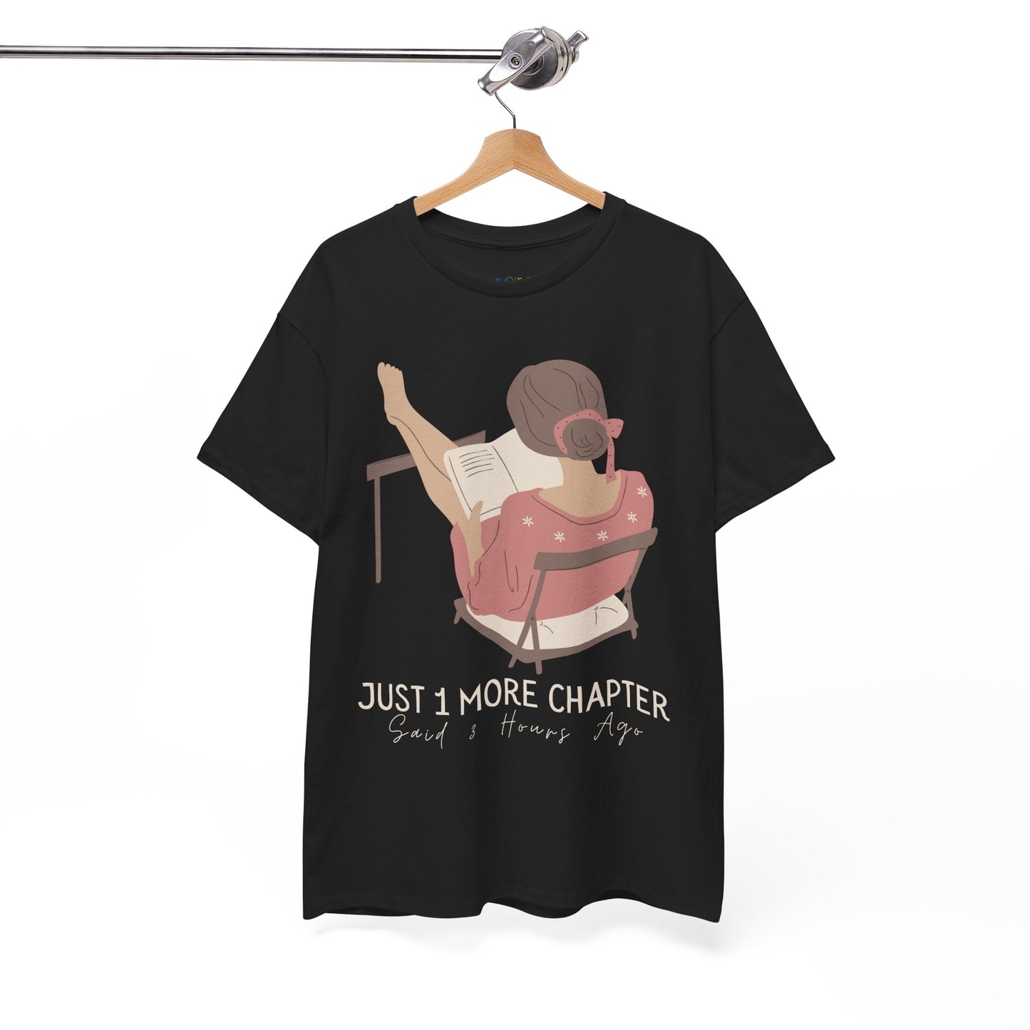 Black t-shirt with a graphic of a person reading a book with her feet propped up and text 'Just 1 More Chapter, Read's Hours Ago' 