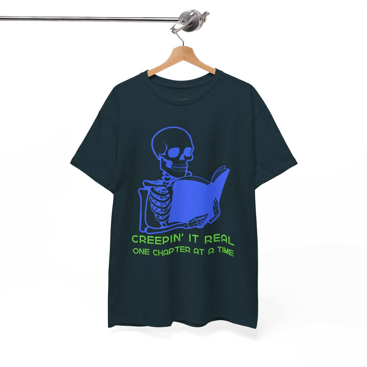Midnight t-shirt with blue skeleton graphic reading a book and green text 'Creepin' It Real One Chapter At A Time' on a hanger against a white background