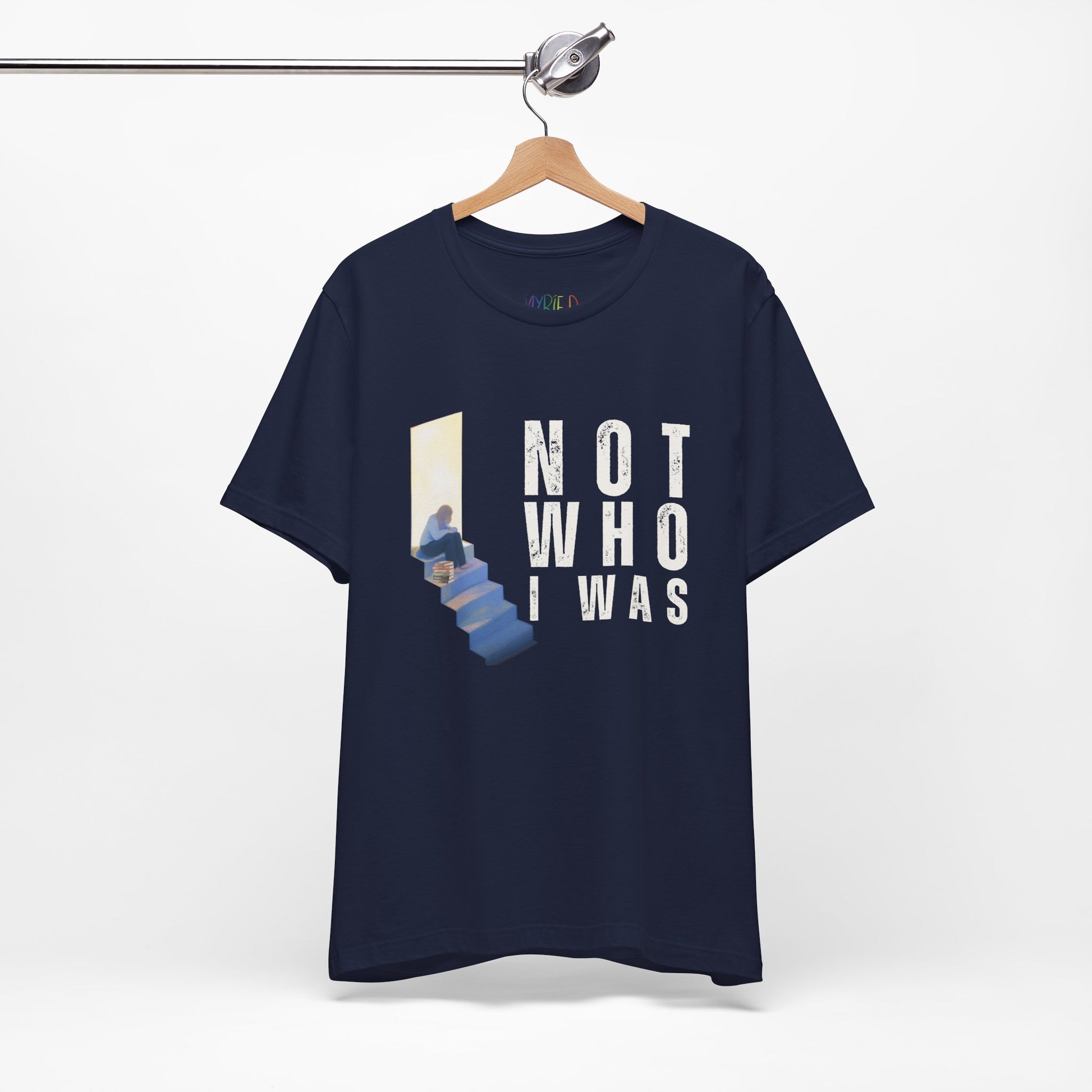 Navy blue t-shirt with person sitting at the top of the stairs, lit from behind and text 'Not Who I Was'