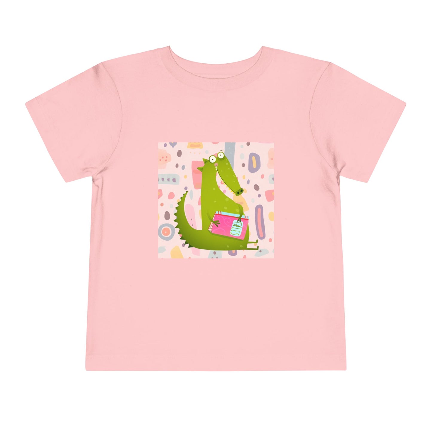 Pink toddler t-shirt with a green gator, holding pink book and colorful pastel background 