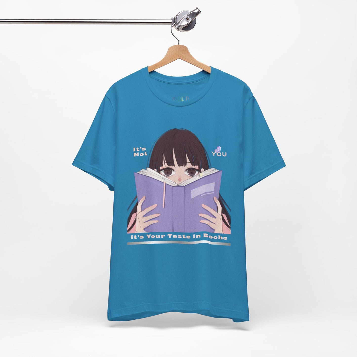 Blue t-shirt with graphic design of a girl peeking over the top of a book and text 'It's Not You. It's Your Taste In Books.'