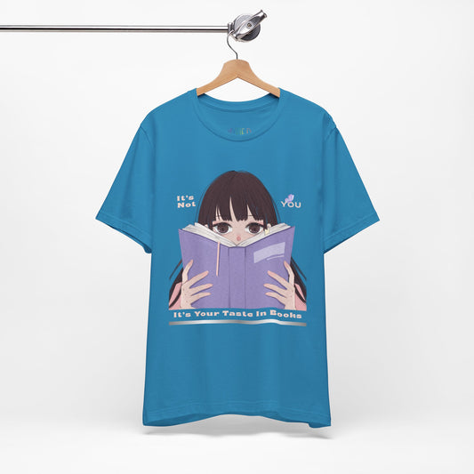 Blue t-shirt with graphic design of a girl peeking over the top of a book and text 'It's Not You. It's Your Taste In Books.'