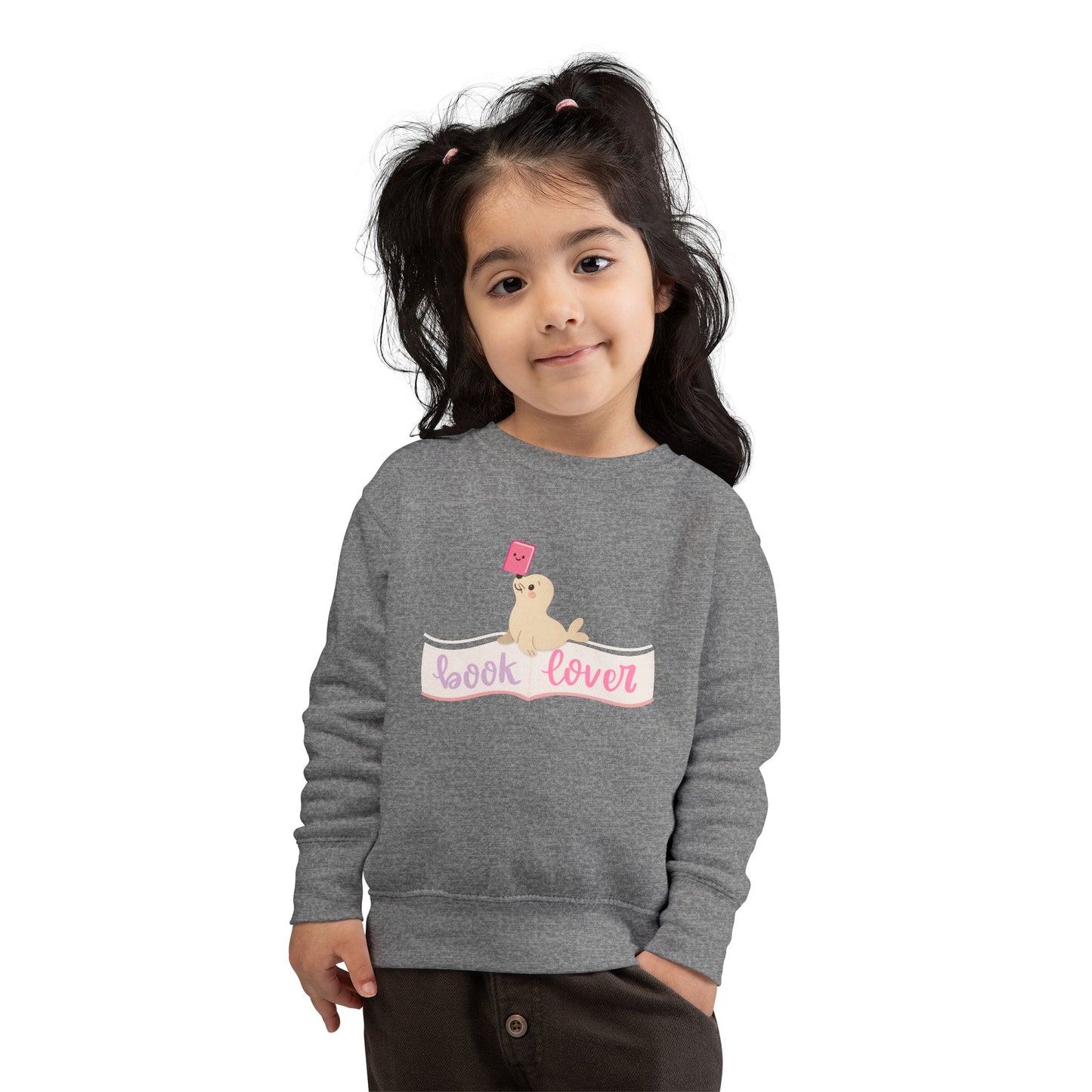 Girl wearing a gray toddler sweatshirt with a seal balancing a book on its nose and 'book lover' 