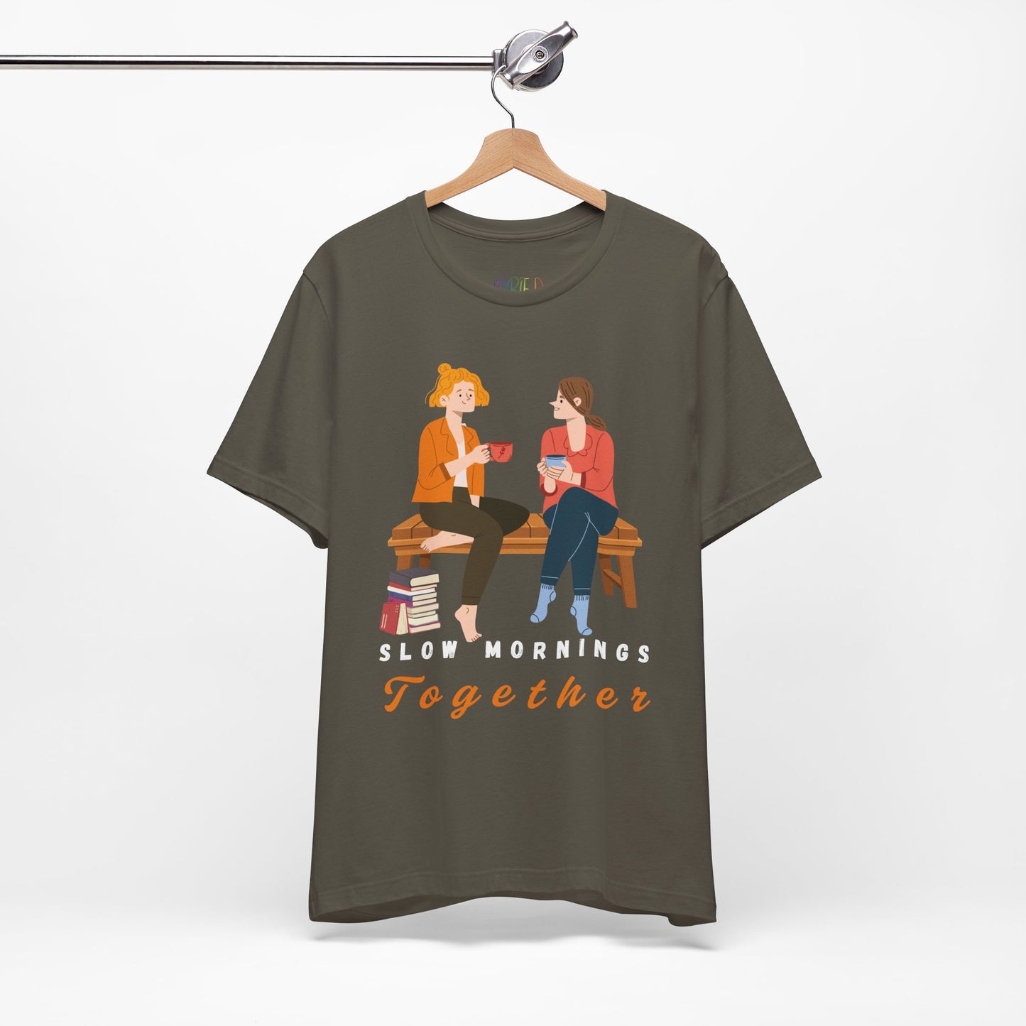 Military green t-shirt with graphic of two people sitting on a bench together, hot beverages in their hands, book at their feet and 'Slow Mornings Together' text below the image
