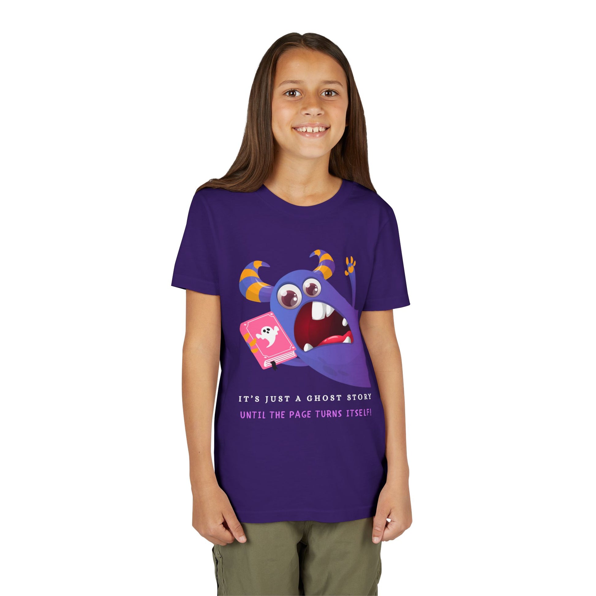 Girl wearing a purple t-shirt with a cartoon monster urgently jumping into frame with a gaping mouth, holding a book and text 'It's Just a Ghost Story Until The Page Turns Itself!'