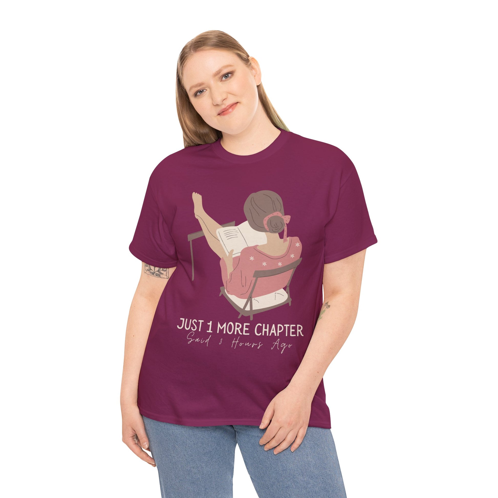 Woman wearing a berry t-shirt with a graphic of a person reading a book with her feet propped up and text 'Just 1 More Chapter, Read's Hours Ago' 
