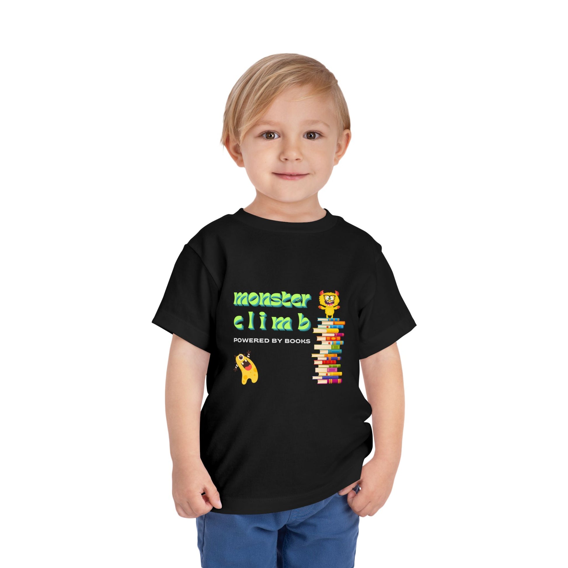 Child wearing a black toddler t-shirt with a monster on top of a colorful stack of books, another monster cheering him on and text 'Monster Climb Powered By Books'