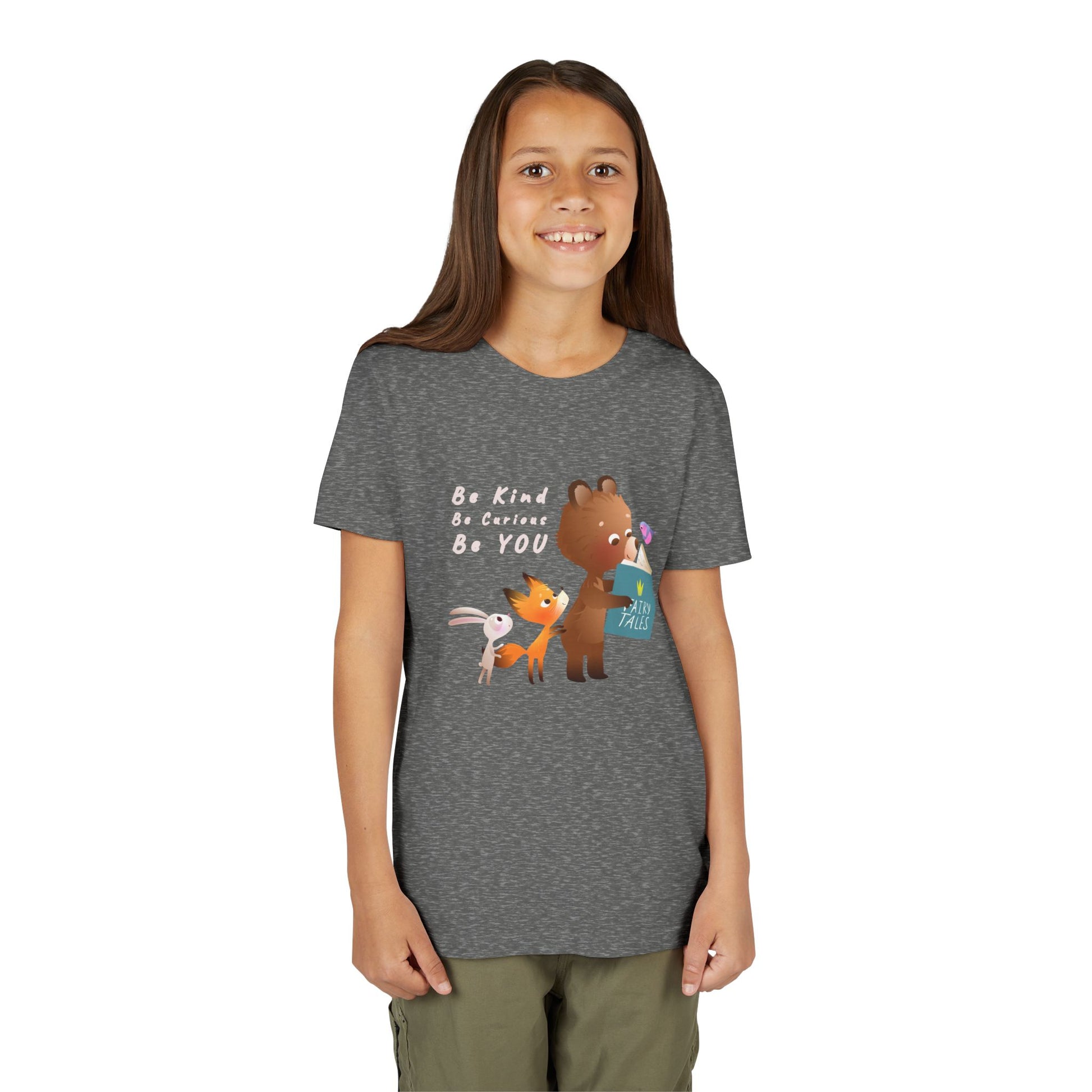 Girl wearing a gray t-shirt with cartoon animals reading a fairy tales book and text 'Be Kind. Be Curious. Be YOU.'