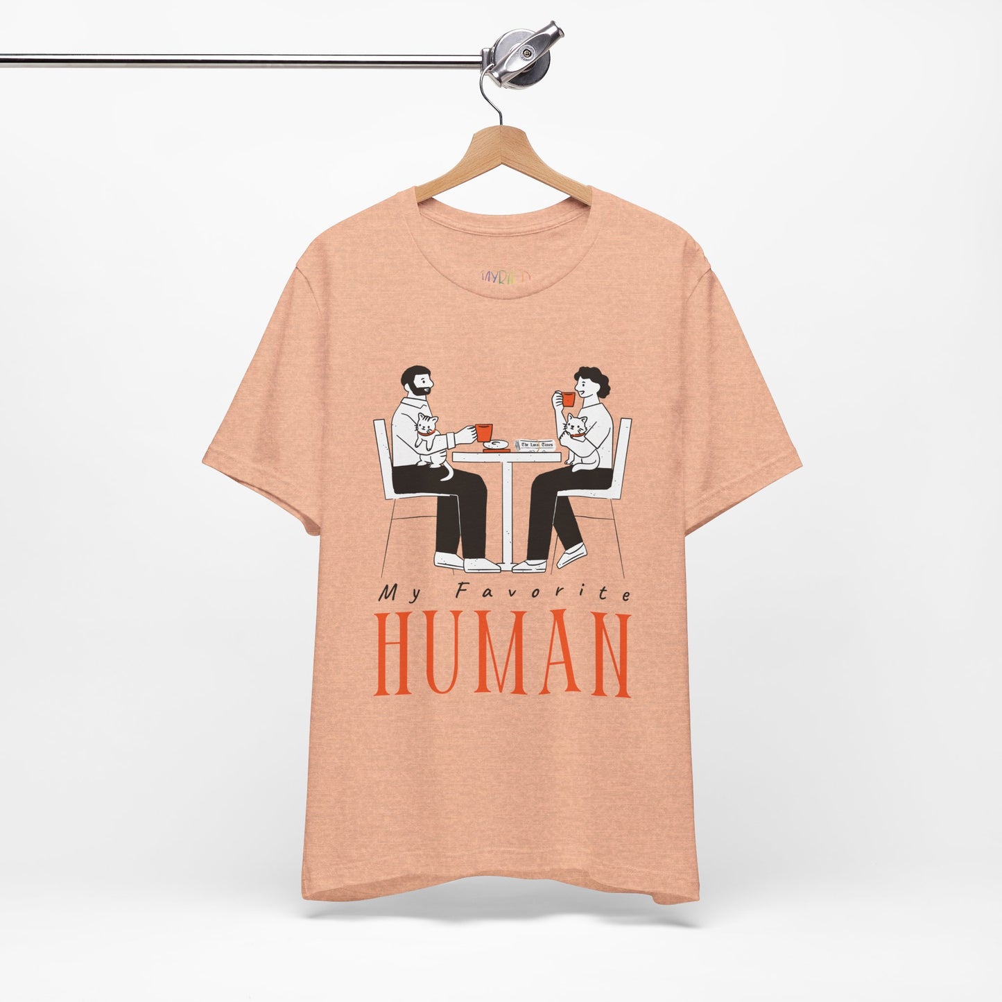 Peach t-shirt with a graphic of two people sitting at a table, newspaper in front of one, drinking hot beverages, holding cats and text 'My Favorite Human' 