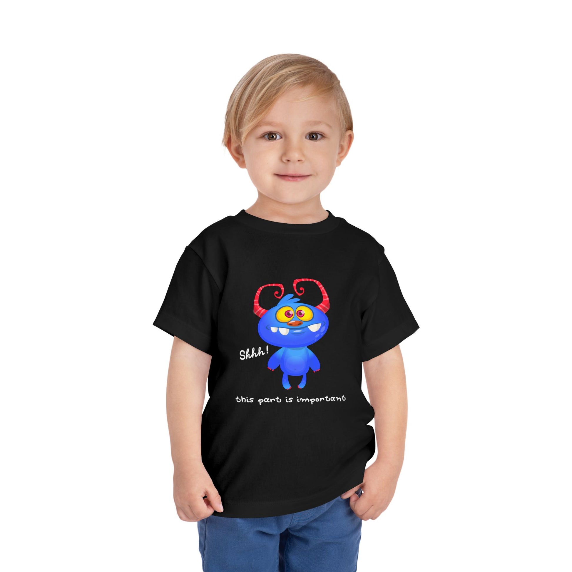 Child wearing a black toddler t-shirt with a blue monster and text 'shhh! this part is important'