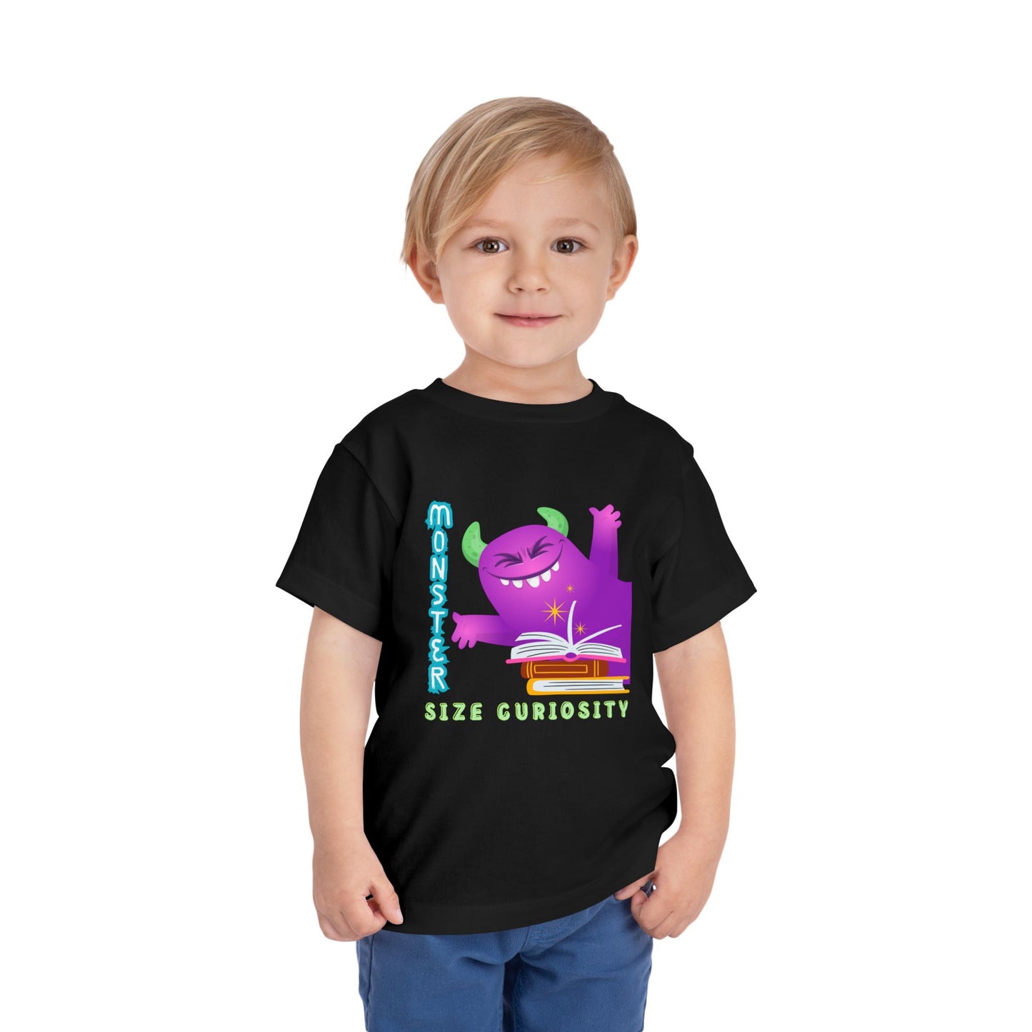 Toddler wearing a black t-shirt with a happy purple monster, a pile of books and text 'Monster Size Curiosity'