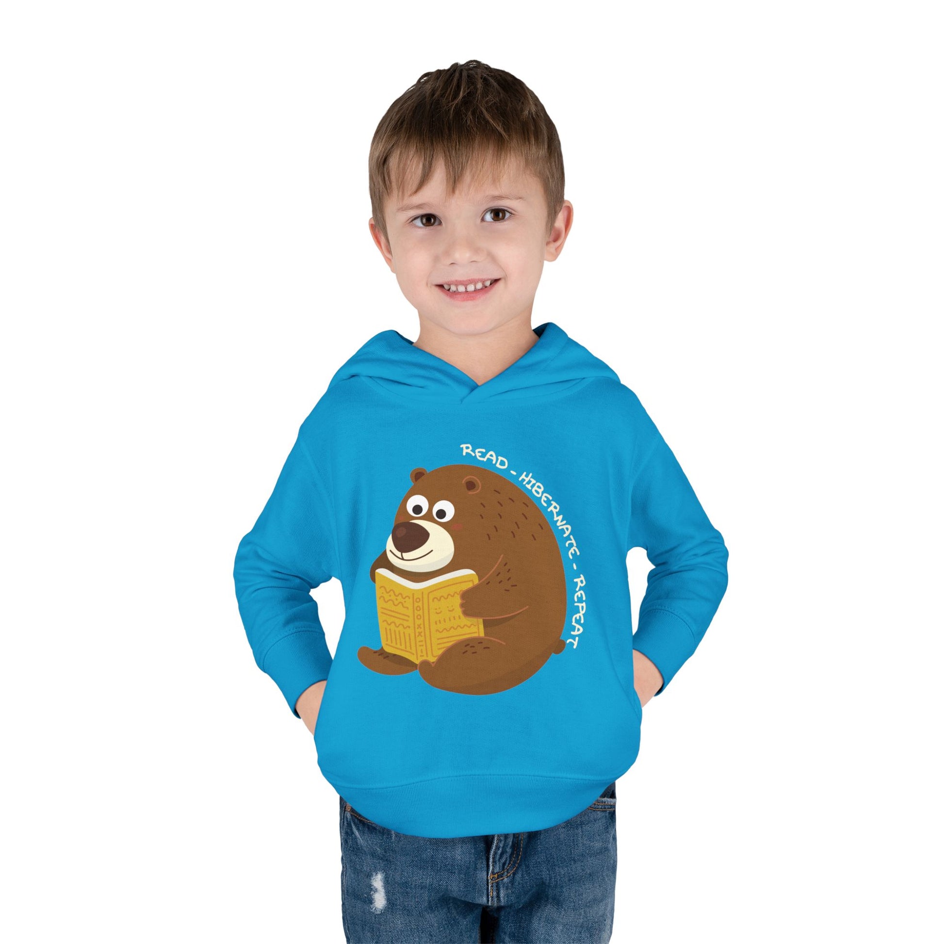 Boy wearing a turquoise toddler hoodie with a bear reading a book graphic and text 'Read, Hibernate, Repeat'